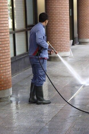 A team member of Alpine Roofing Construction in the process of power washing a sidewalk